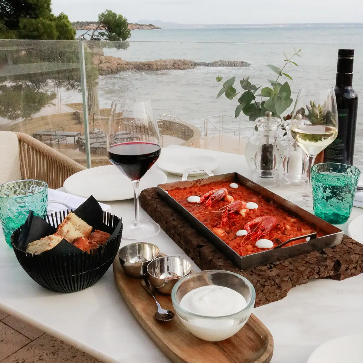 Mesa junto al mar: vino tinto y plato con langostinos sobre plancha de panque.