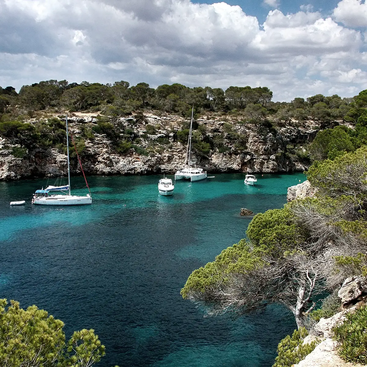 Bah&iacute;a con barcos fondeados entre rocas y vegetaci&oacute;n, agua turquesa