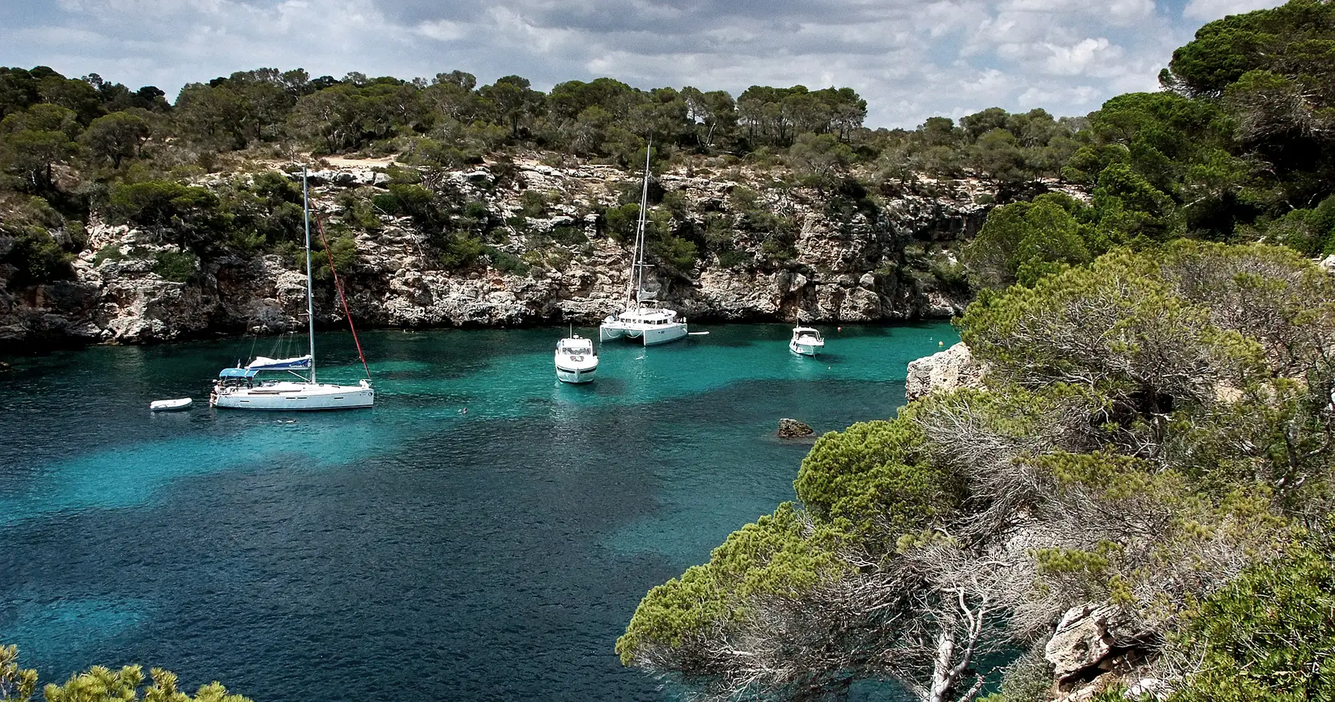 Bah&iacute;a con barcos de vela anclados en aguas turquesa, rodeada de vegetaci&oacute;n