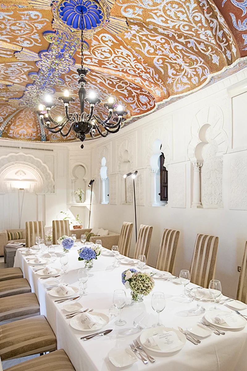 Sala elegante con mesa puesta, l&aacute;mpara de ara&ntilde;a y techo decorado con azulejos.