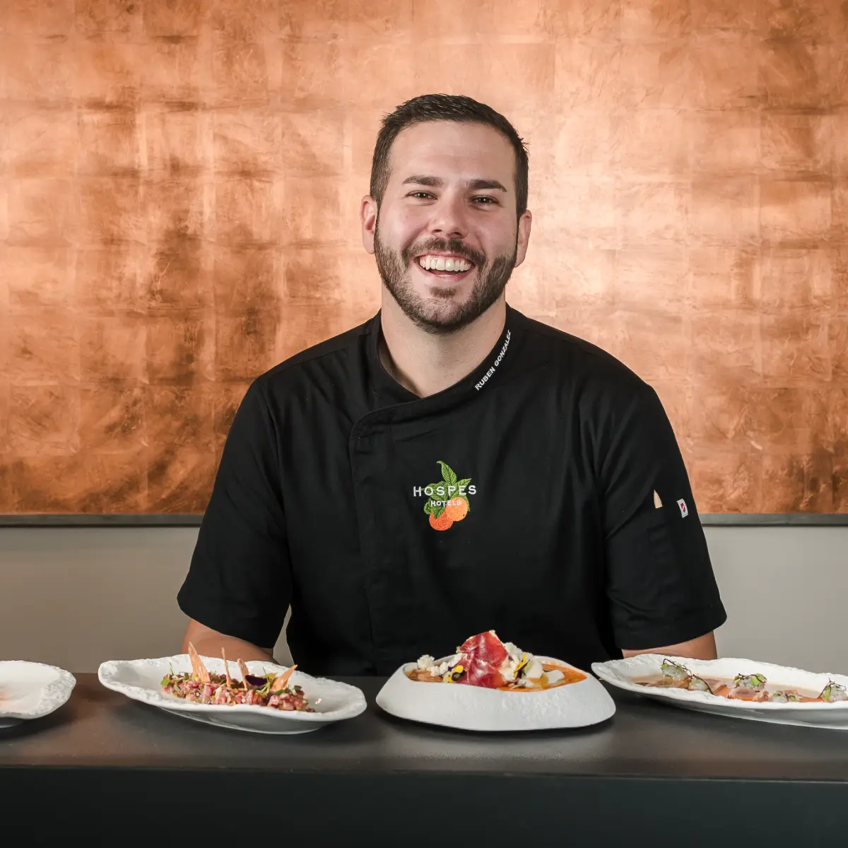 Chef sonriente en restaurante, posando con platos de comida al frente