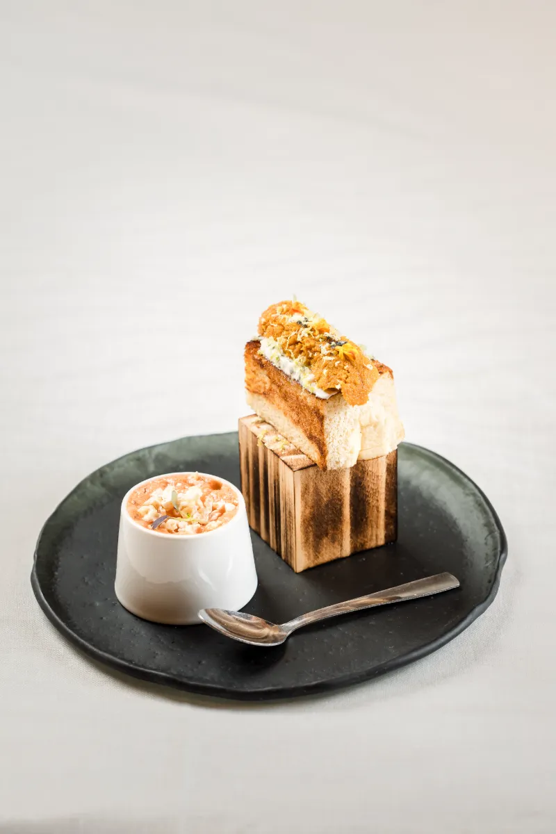 Rebanada de bizcocho con crema y crumble, con salsa en vasito y cuchara