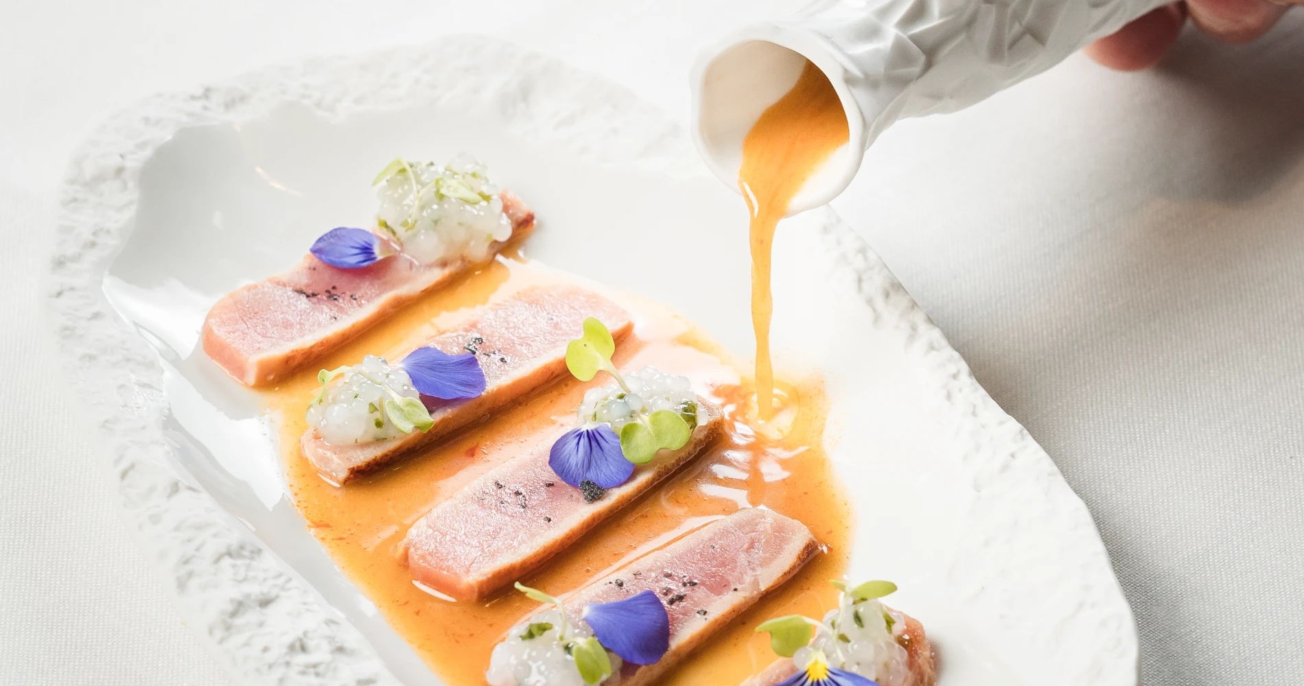 At&uacute;n sellado en salsa con flores y microvegetales, servido en plato blanco.
