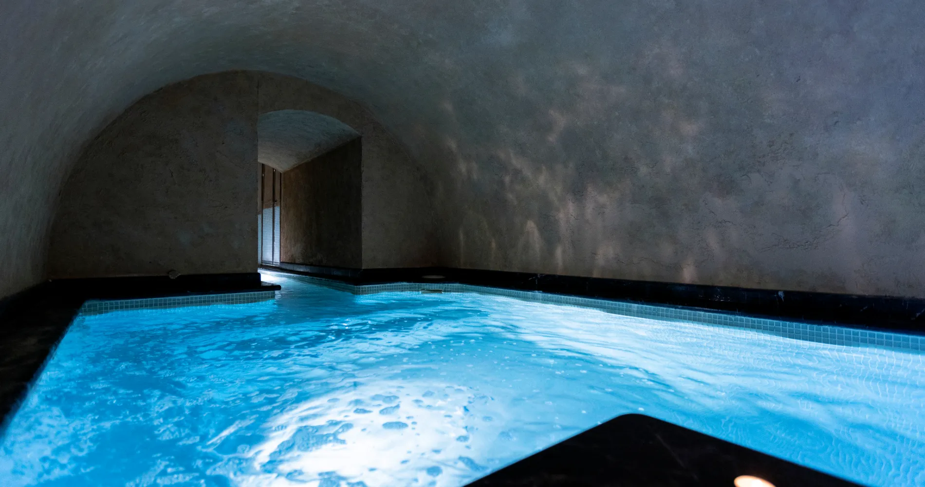 Piscina de interior con agua azul y nicho de piedra con luz natural