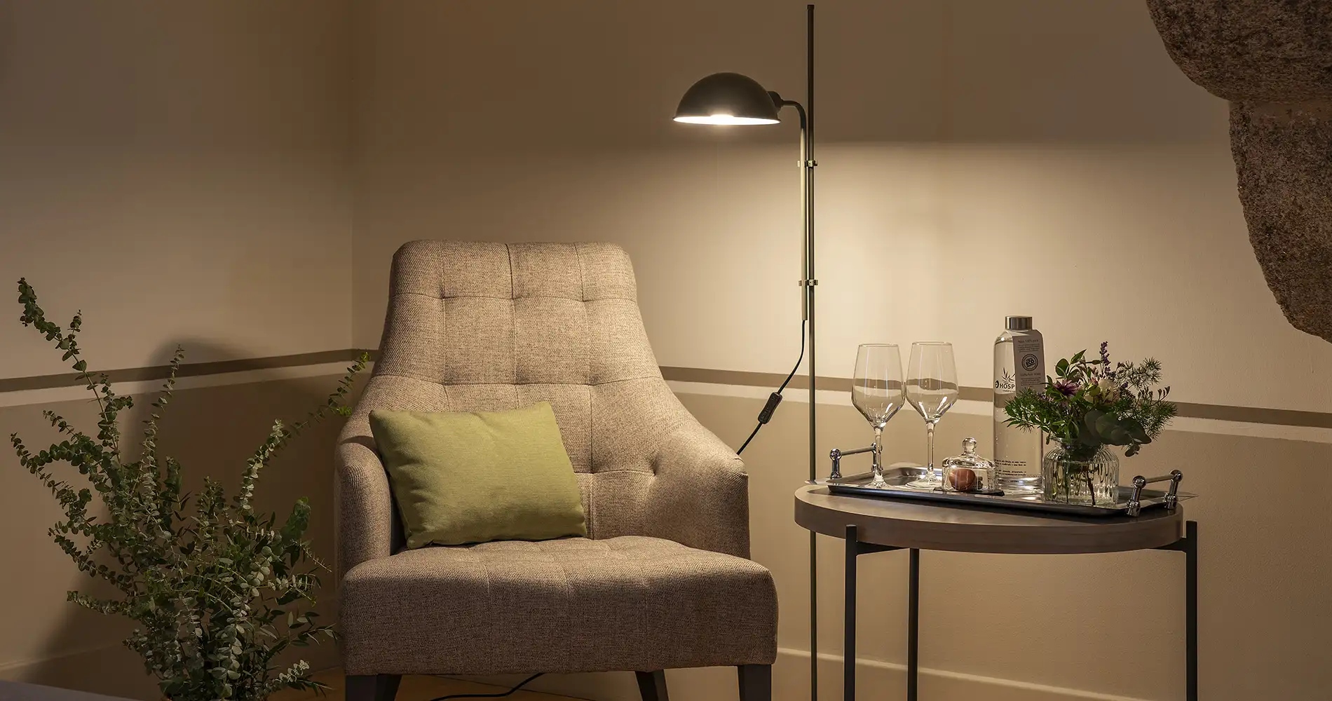 Sill&oacute;n de tela beige con l&aacute;mpara y mesa con copas en interior c&aacute;lido