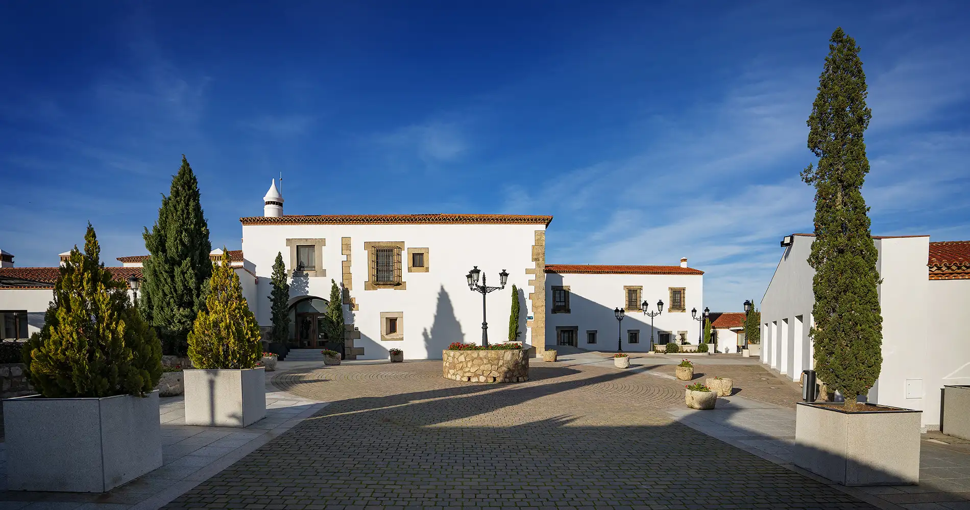 Patio con casa blanca de estilo colonial, cipreses y cielo azul despejado
