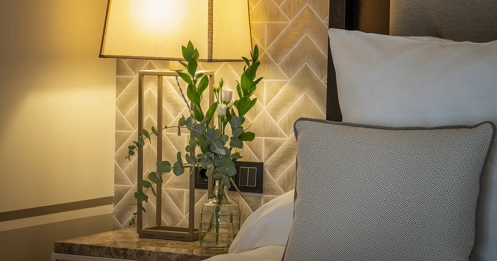 Arreglo de eucalipto verde en mesa con l&aacute;mpara y coj&iacute;n decorativo gris