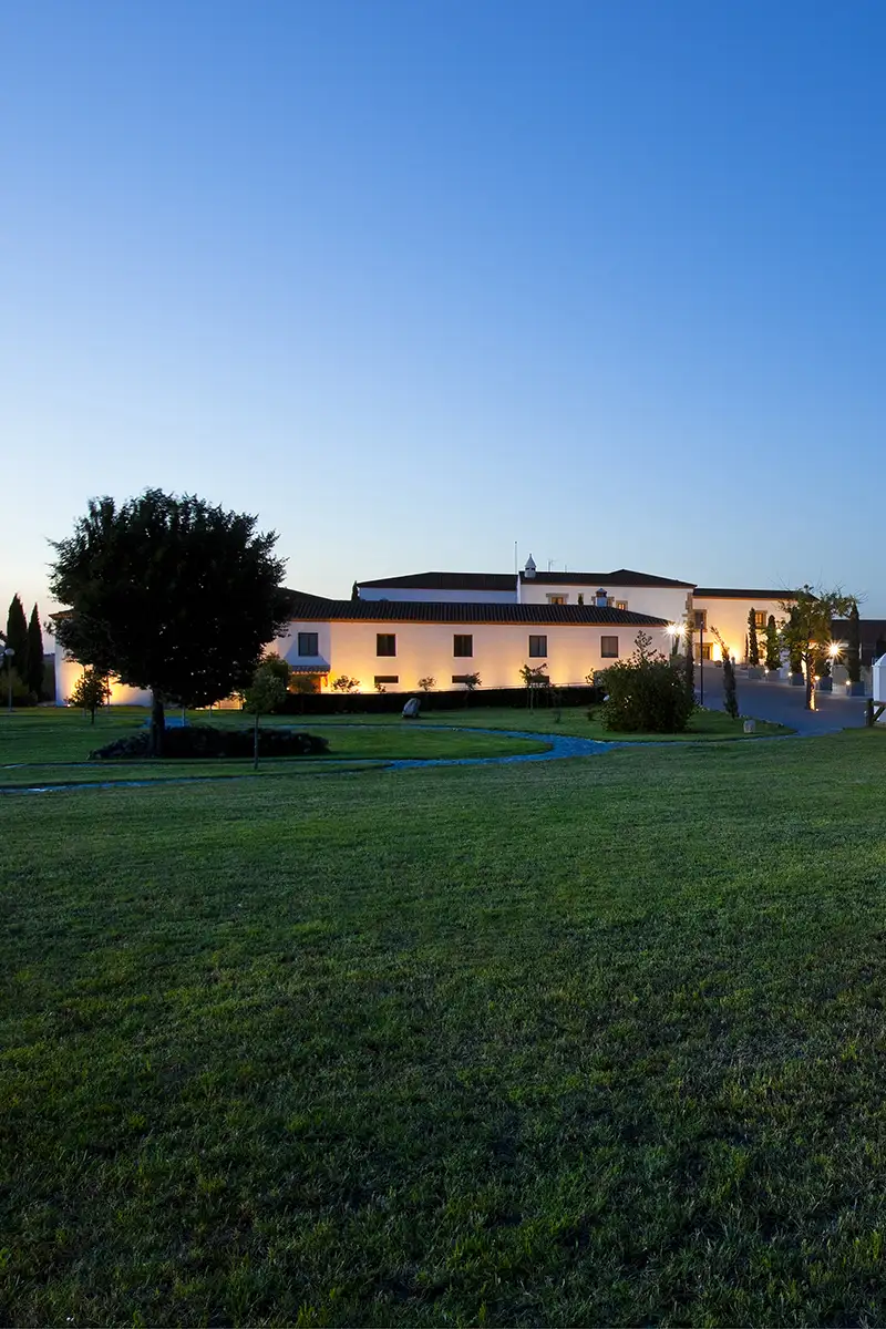 Fachada de edificio blanco iluminado al atardecer con jard&iacute;n y c&eacute;sped
