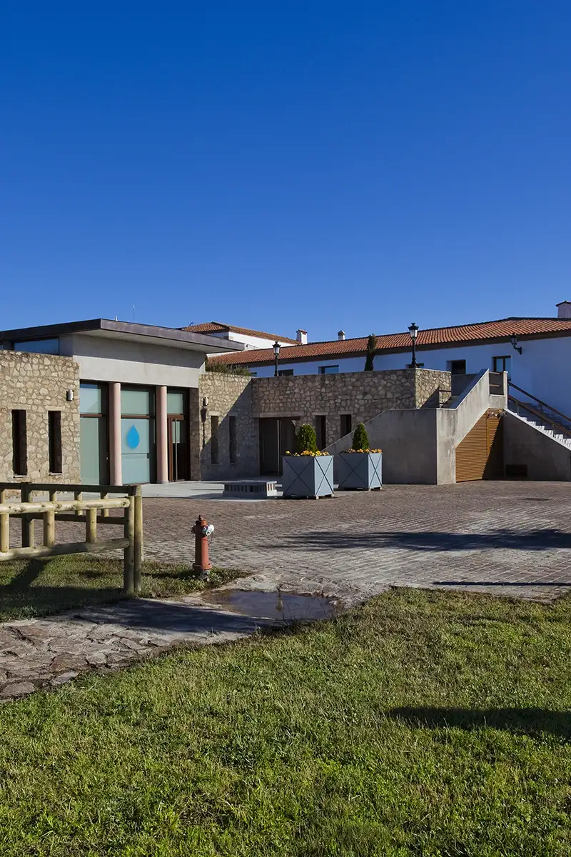 Patio con c&eacute;sped y edificios de piedra, azul cielo despejado y macetas