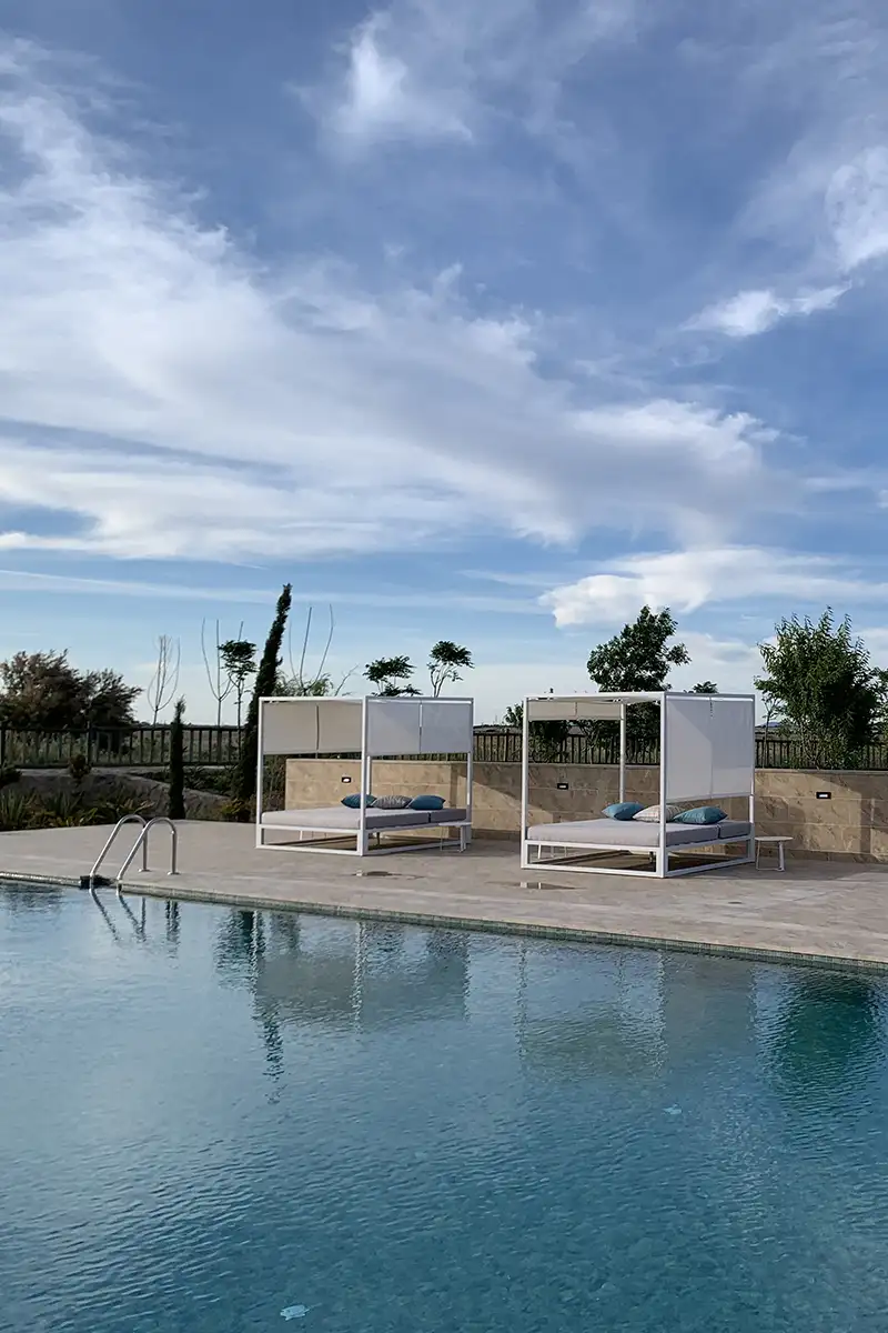 Piscina con tumbonas blancas y cojines azules, cielo nublado.
