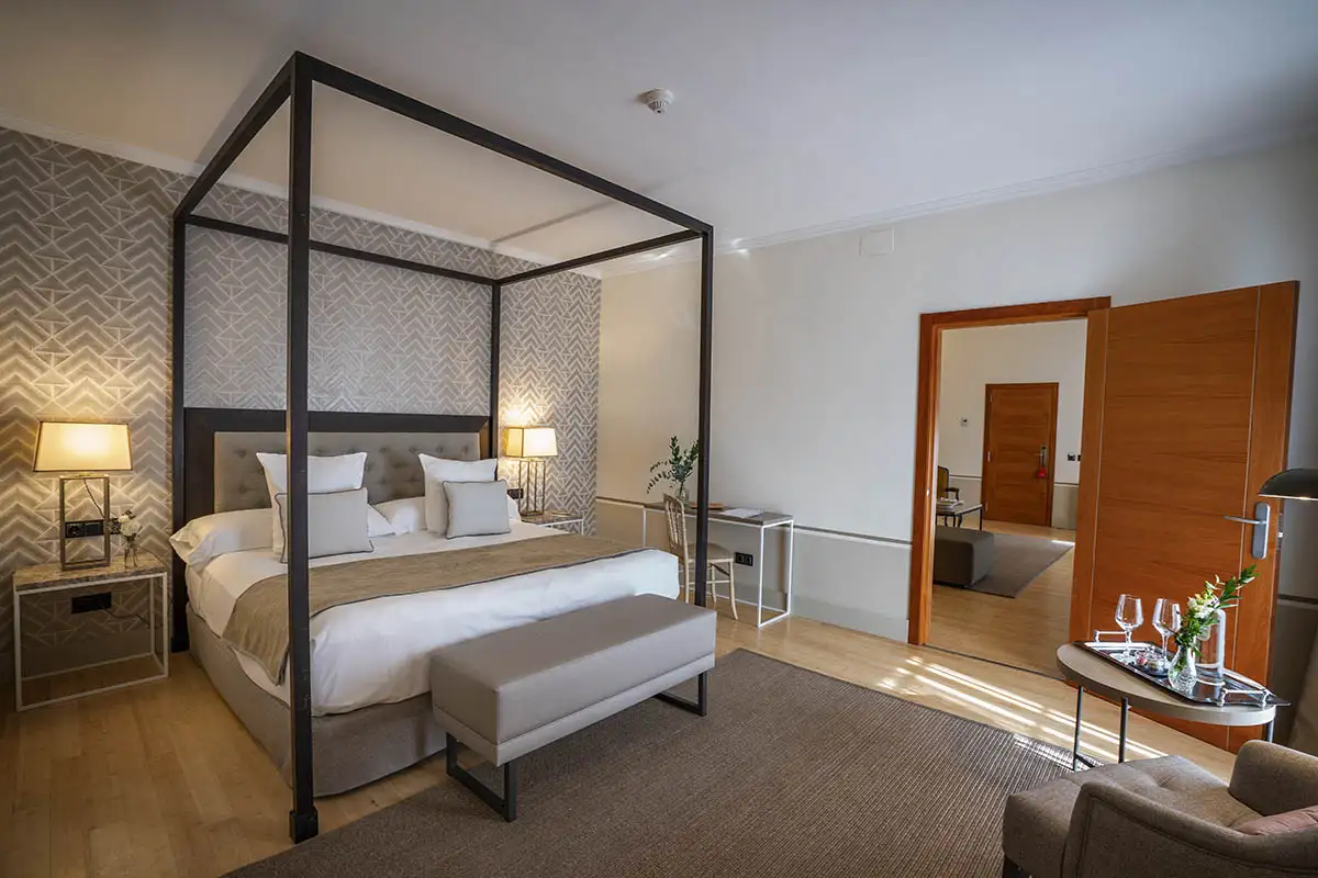 Habitaci&oacute;n hotelera moderna con cama con dosel y sala de estar al fondo