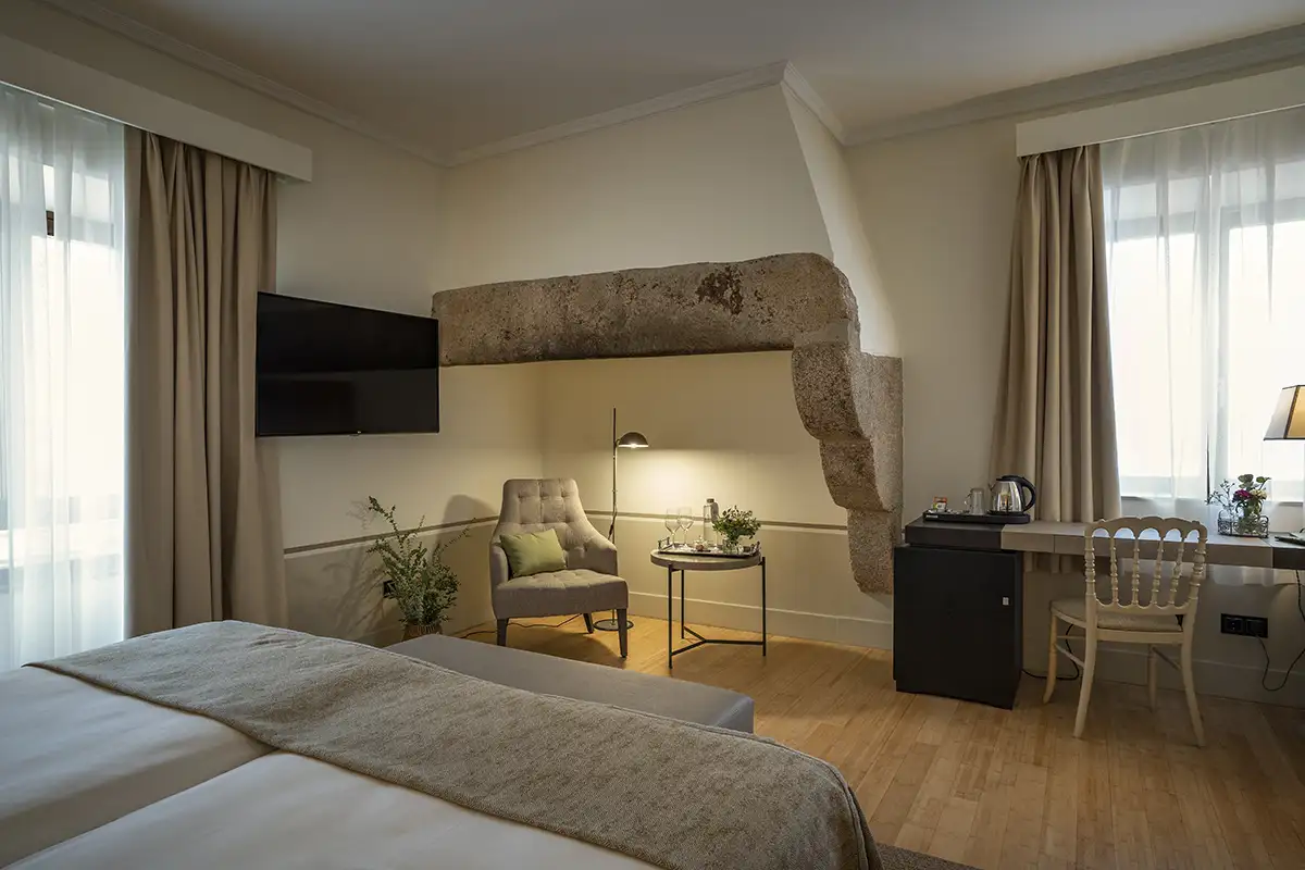 Dormitorio moderno con cama, TV, l&aacute;mparas y pared de piedra junto a ventanas