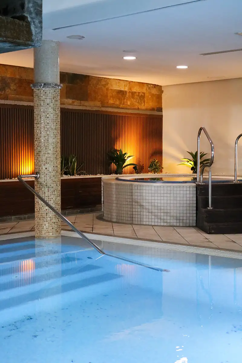 Piscina interior con cascada y zona de hidromasaje iluminada.
