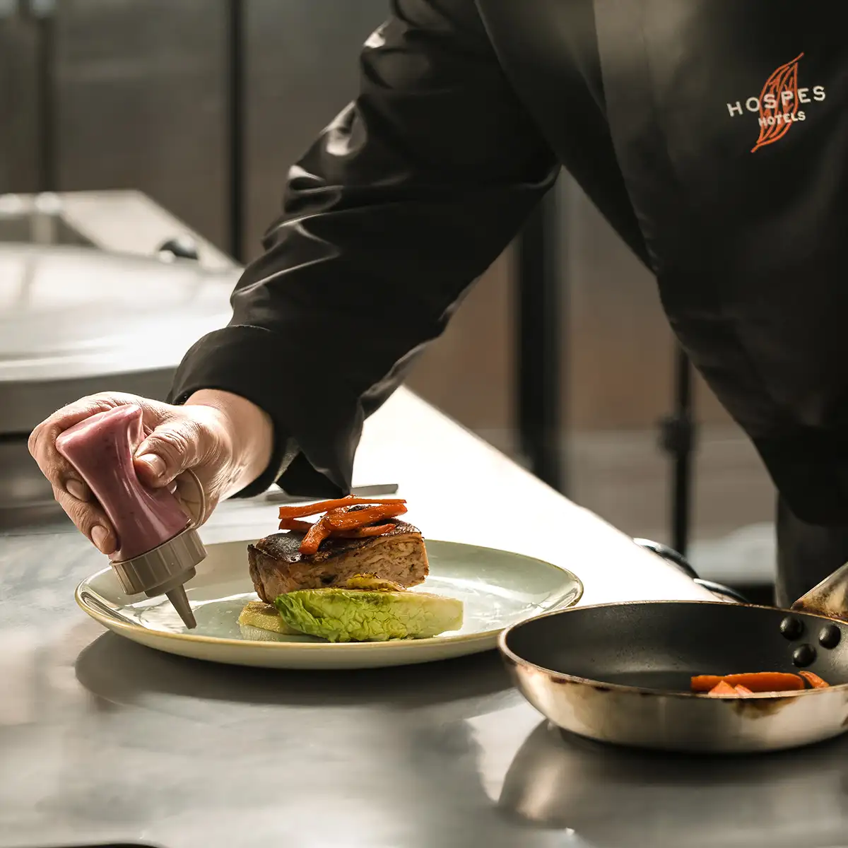 Chef emplatando carne con zanahorias y guarnici&oacute;n verde en plato blanco