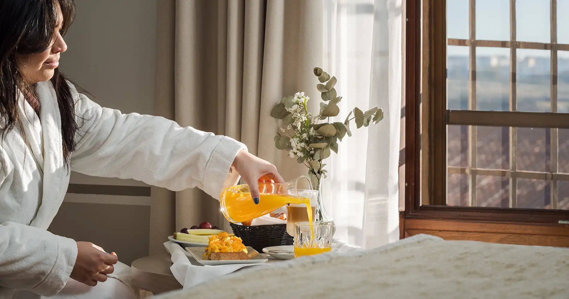 Mujer sirve jugo de naranja en la mesa junto a una ventana y flores