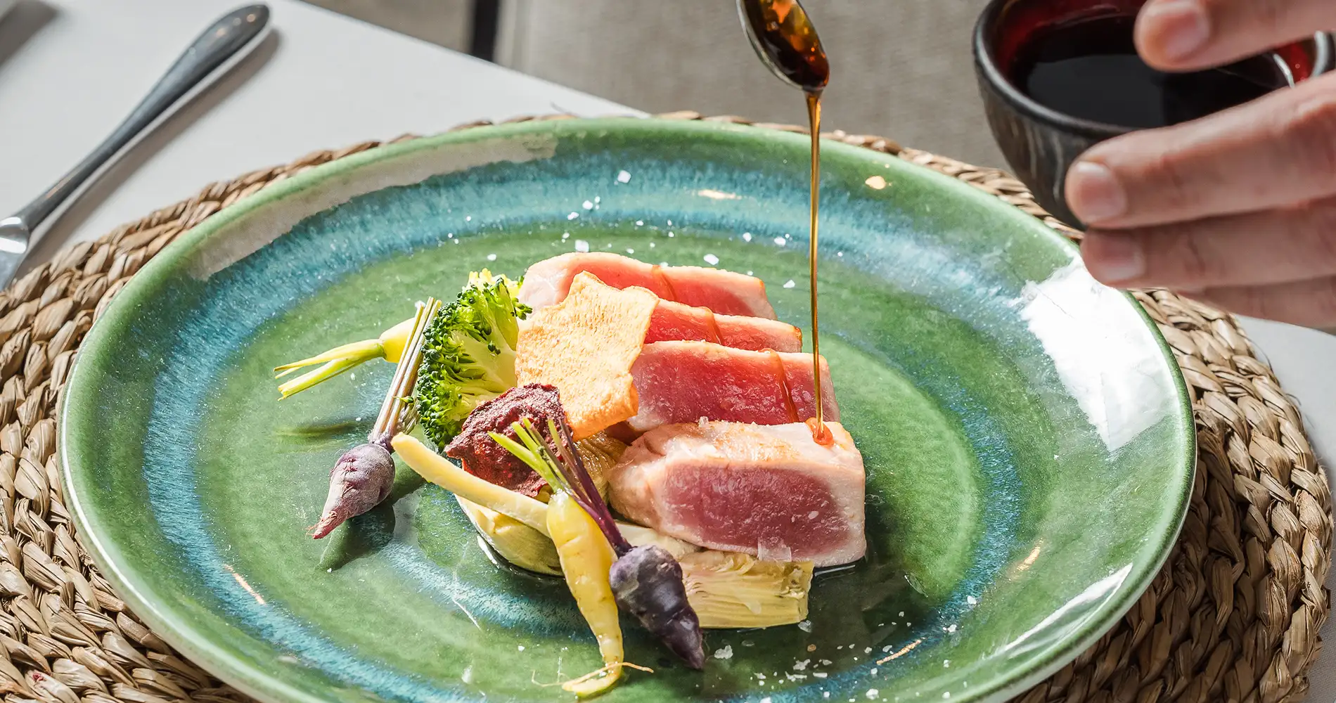 Plato verde con verduras y carne, aceite dorado cayendo desde una cuchara