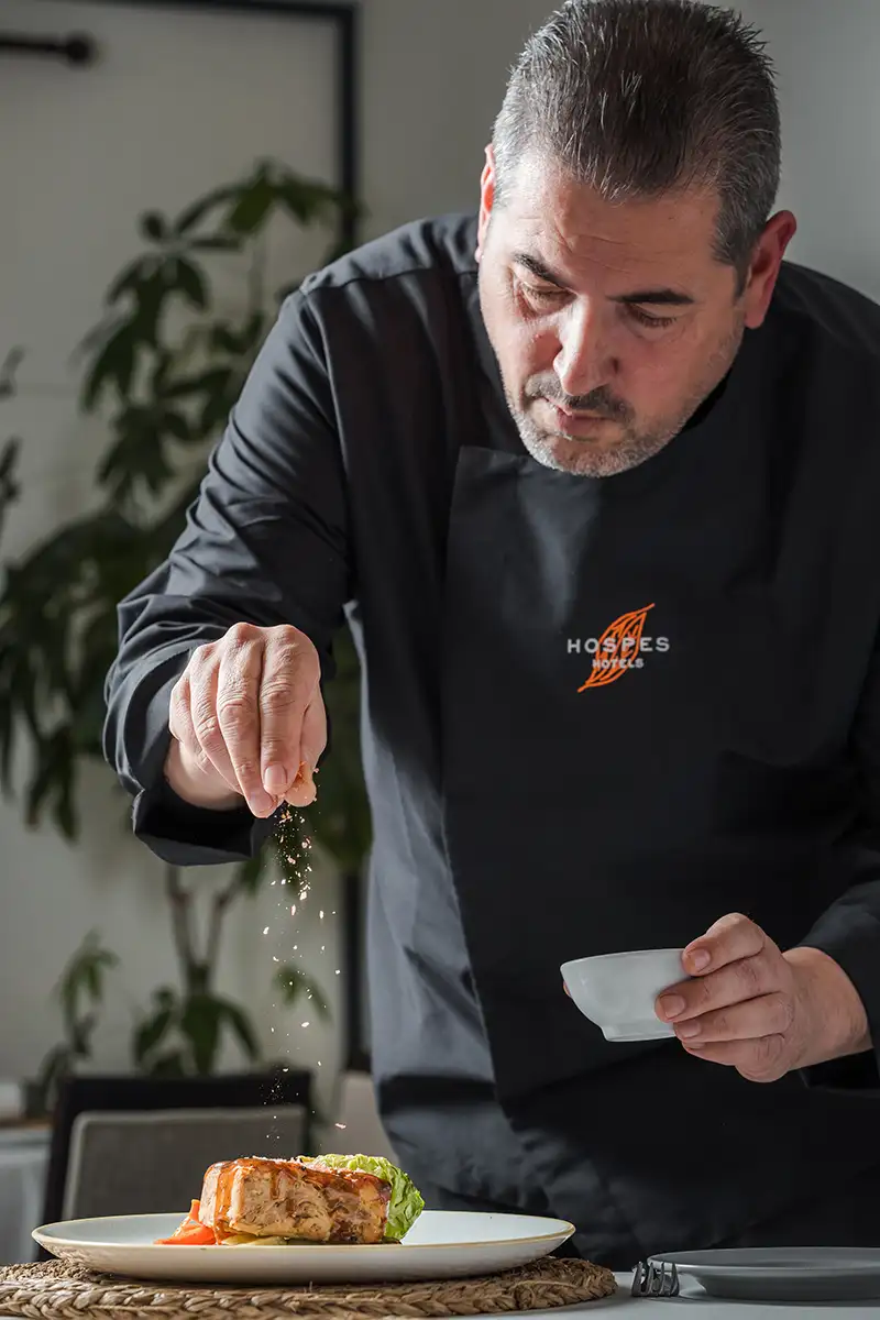 Chef corta un plato con chispas sobre una mesa, en interior.