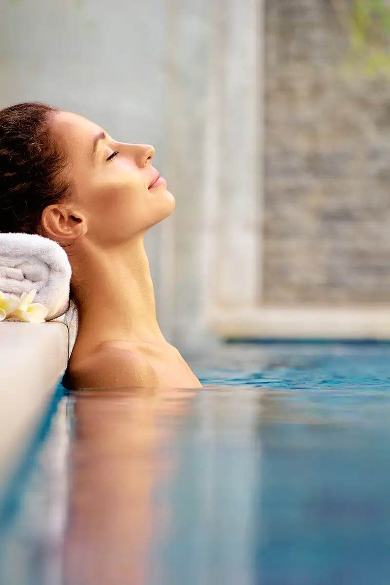 Mujer relaj&aacute;ndose en piscina con toalla en el cuello, mirando al frente