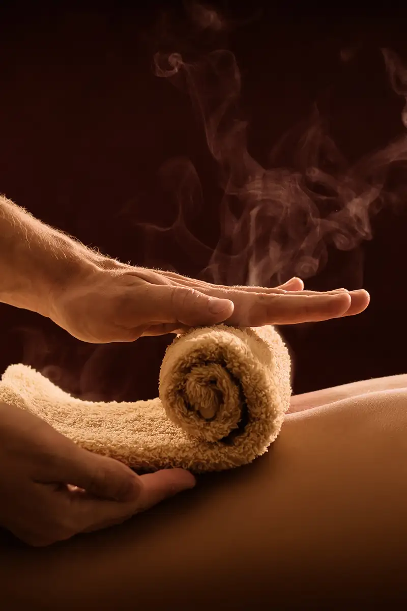 Manos sostienen una toalla enrollada con vapor, escena de spa relajante