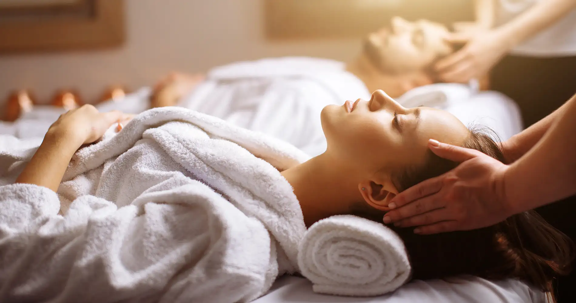 Masaje relajante a una mujer en la cama, con toallas y manos sobre su rostro