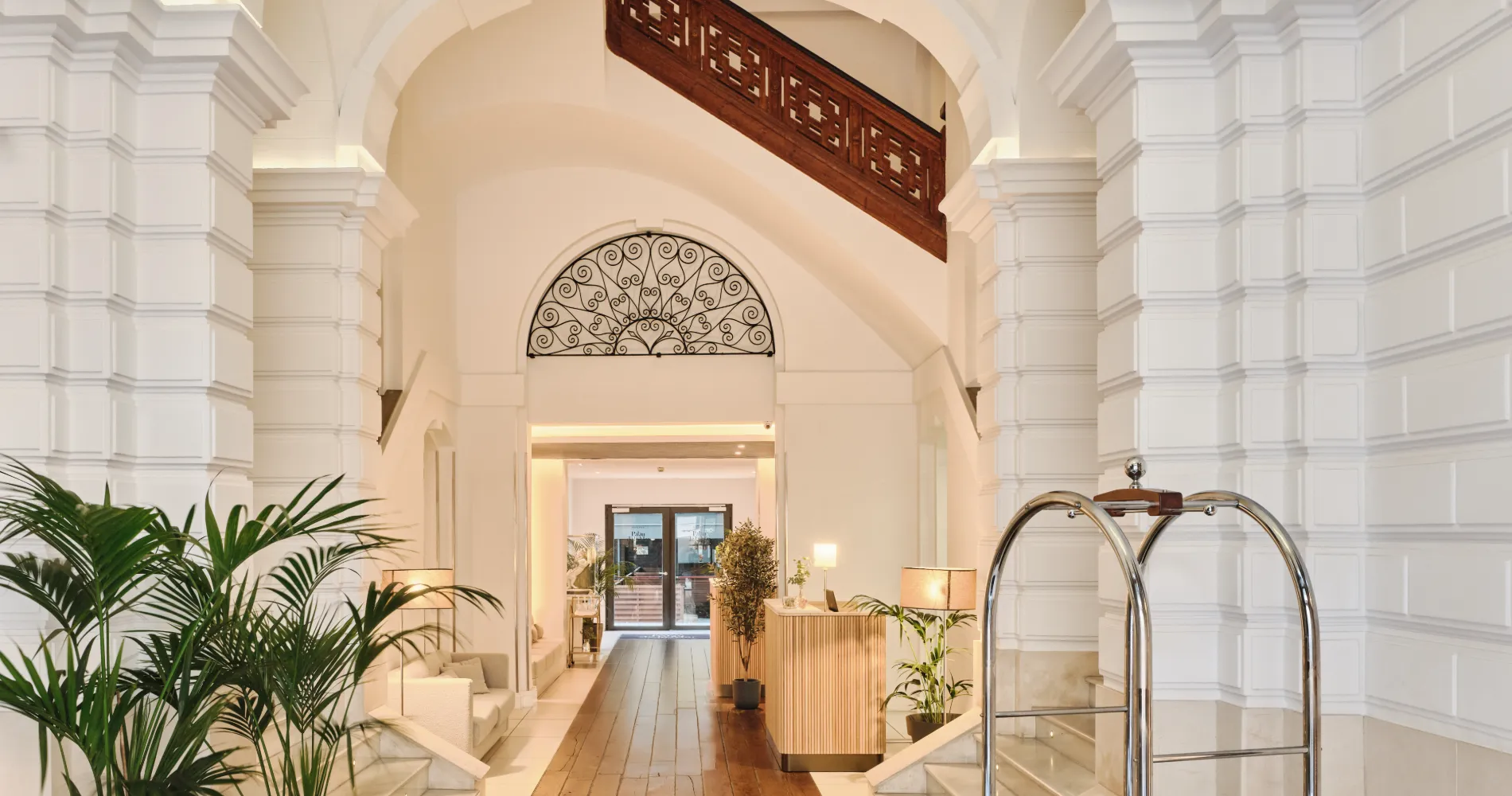 Lobby elegante con arcos, barandales de madera y plantas, interior iluminado