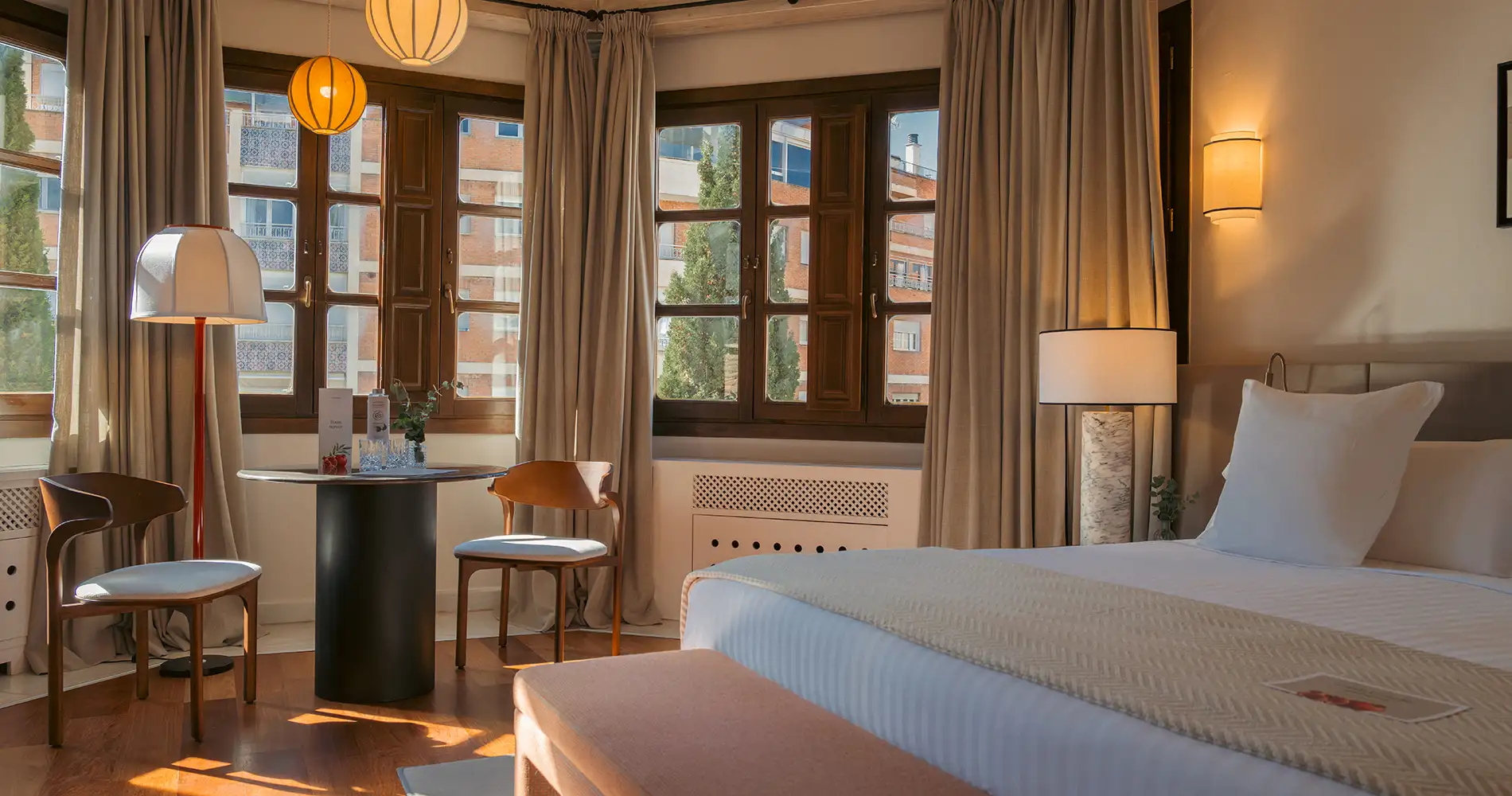 Habitaci&oacute;n de hotel luminosa con cortinas, cama y l&aacute;mparas colgantes doradas