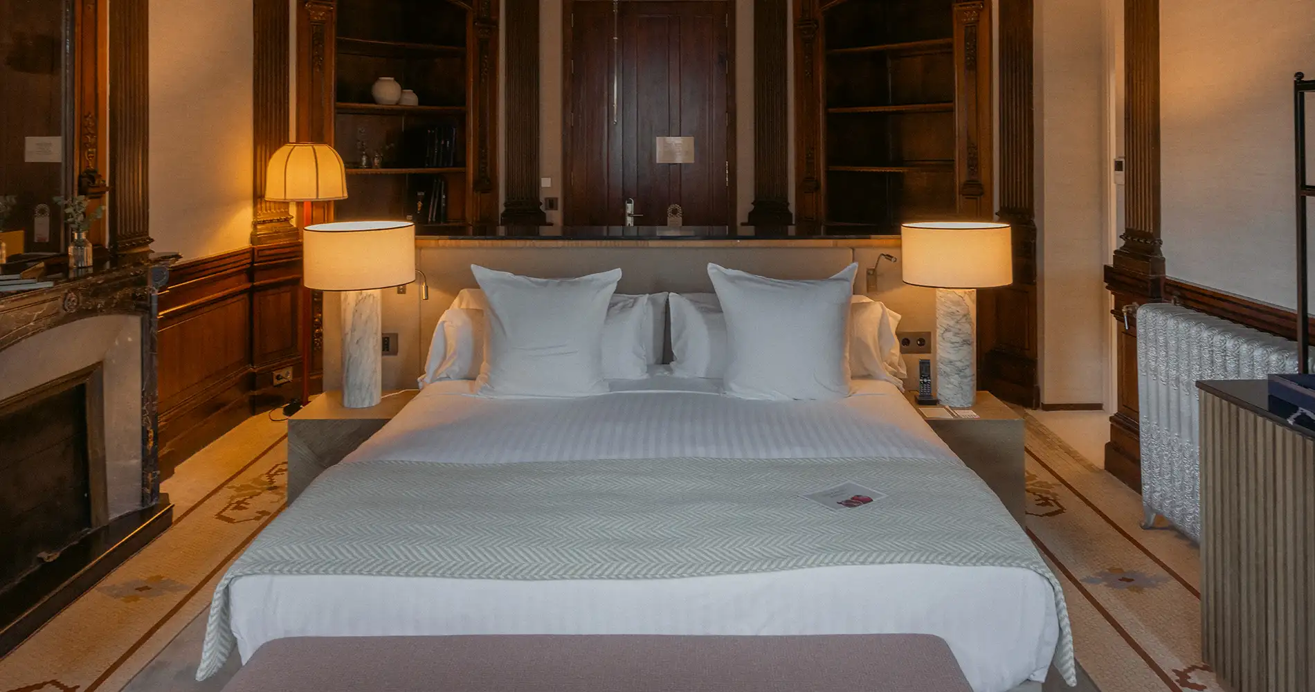 Dormitorio elegante con cama doble blanca, dos l&aacute;mparas y muebles de madera