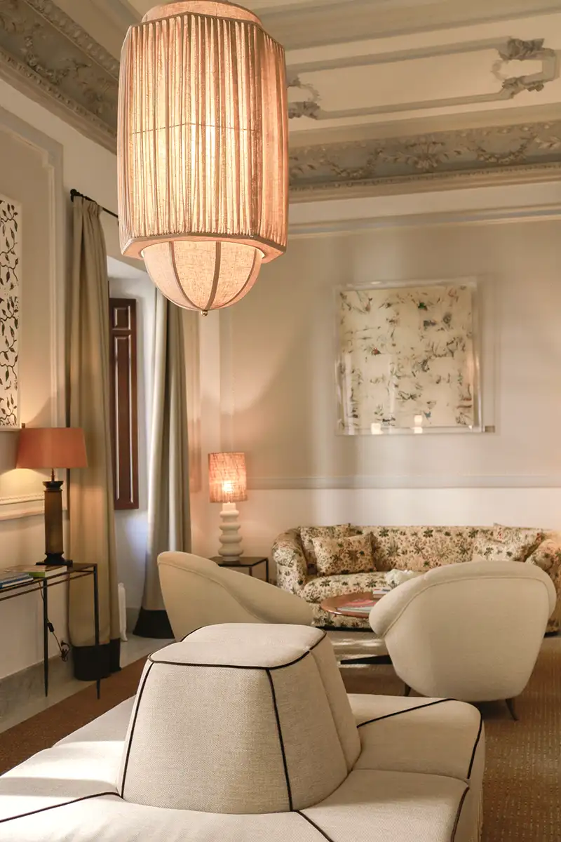 Sala de estar con l&aacute;mpara colgante de mimbre y sillones beige claros.