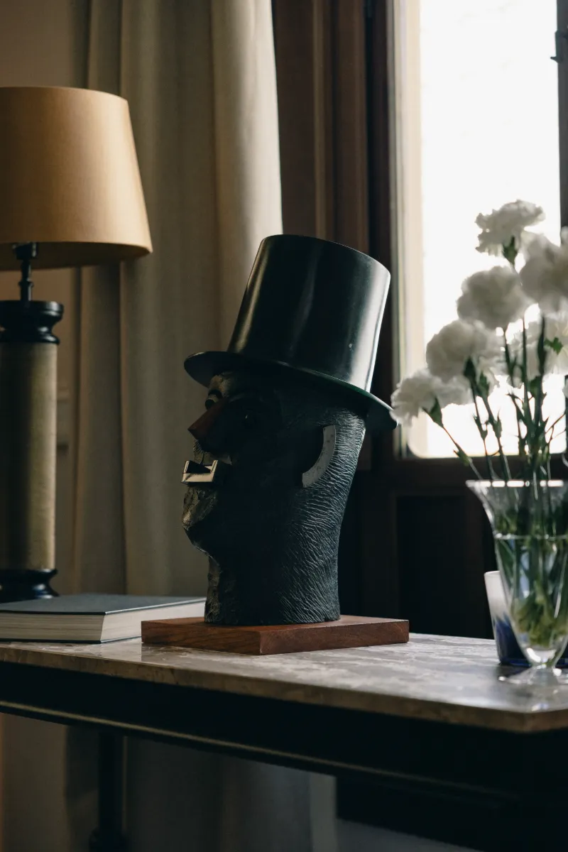 Retrato de una figura con sombrero negro sobre una mesa junto a un jarr&oacute;n con flores
