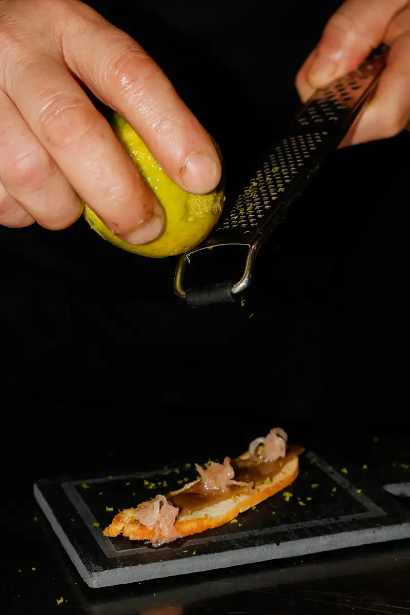 Manos cortando un taco amarillo con lim&oacute;n sobre plancha negra caliente