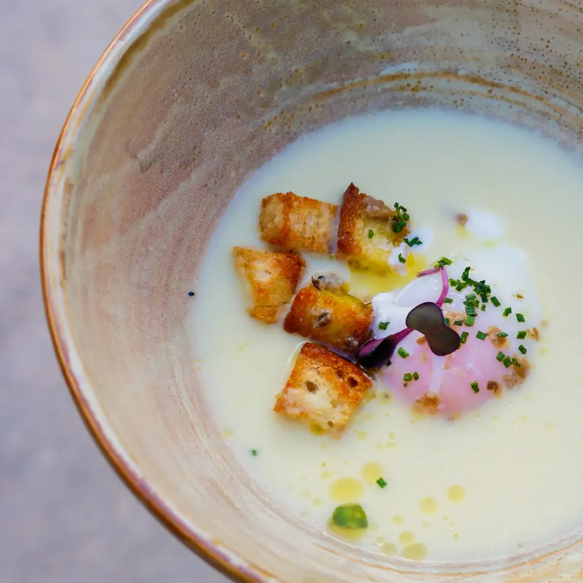 Sopa cremosa con crutones, cebolla morada y hierbas frescas en plato blanco