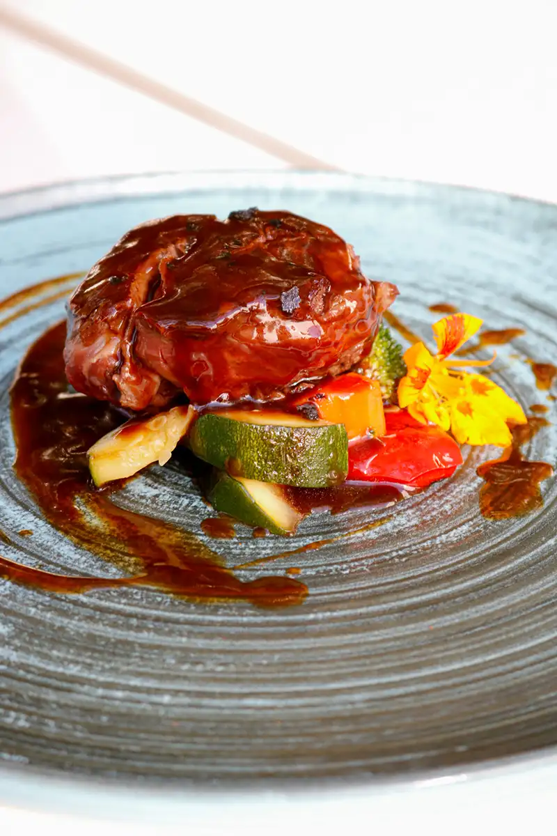 Carne estofada con verduras y flor comestible en plato.