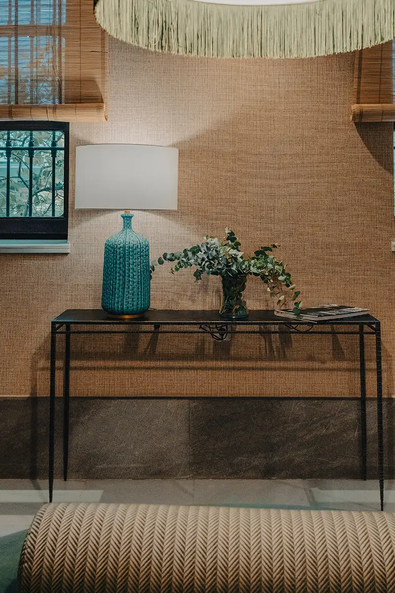 Sala con mesa de hierro, l&aacute;mpara blanca y jarr&oacute;n azul con plantas verdes