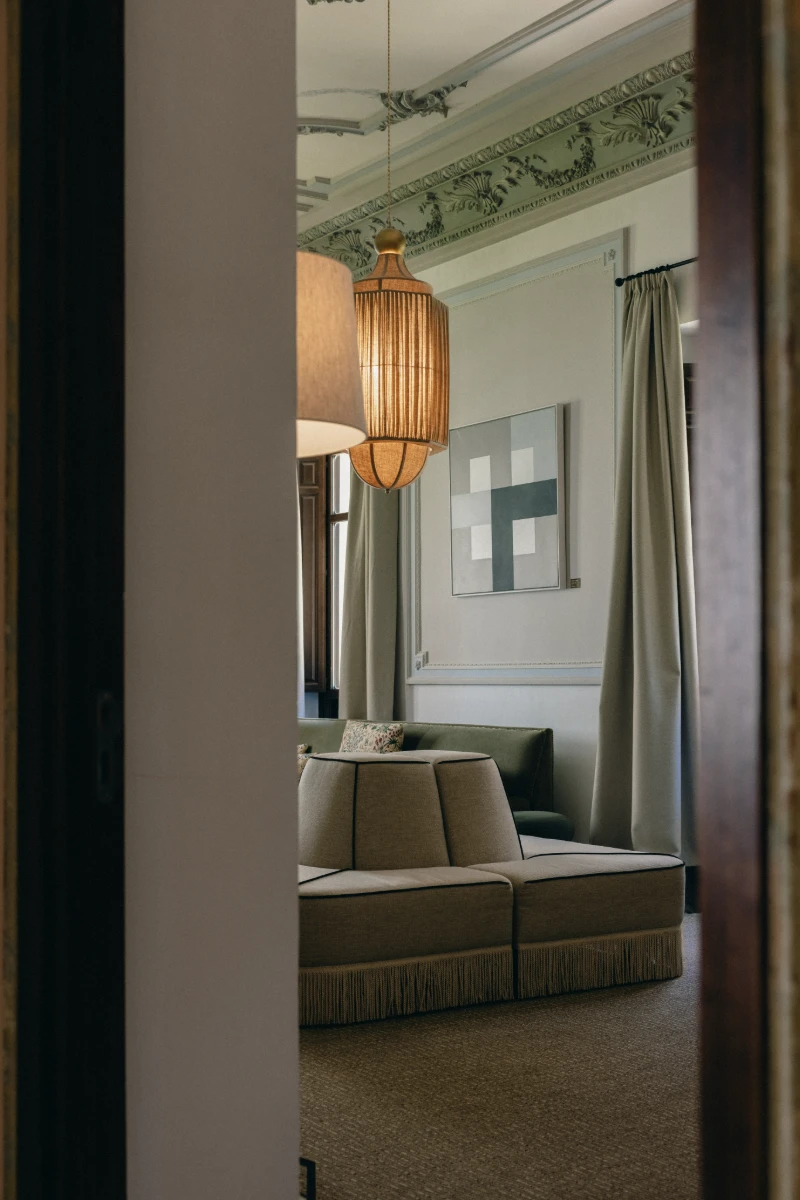 Sala de estar elegante con sof&aacute;, cortinas y l&aacute;mparas doradas, vista desde puerta