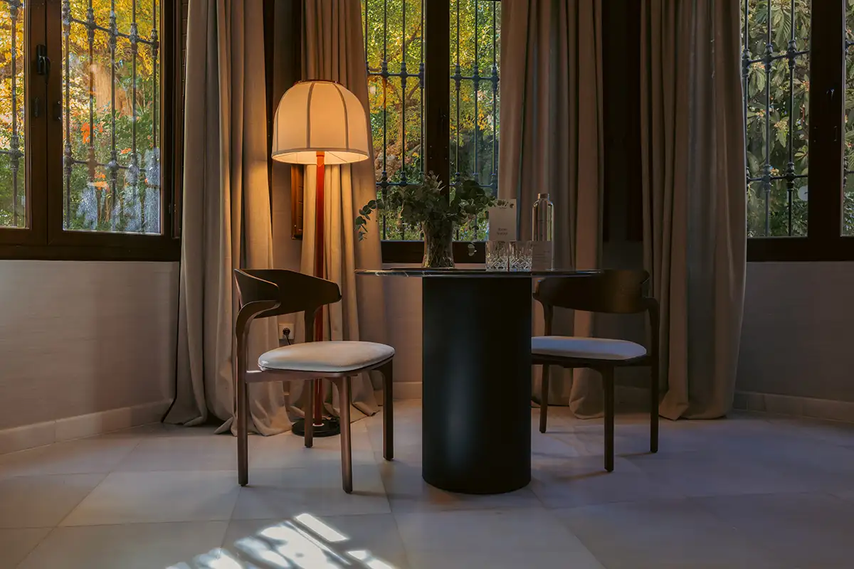 Sala moderna con l&aacute;mpara de mesa y cortinas frente a ventana con luz c&aacute;lida.