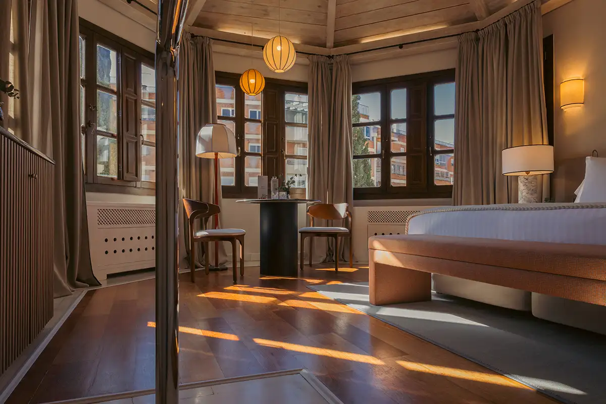 Interior moderno con cama, mesas y sillas, ventanas y cortinas, luz c&aacute;lida