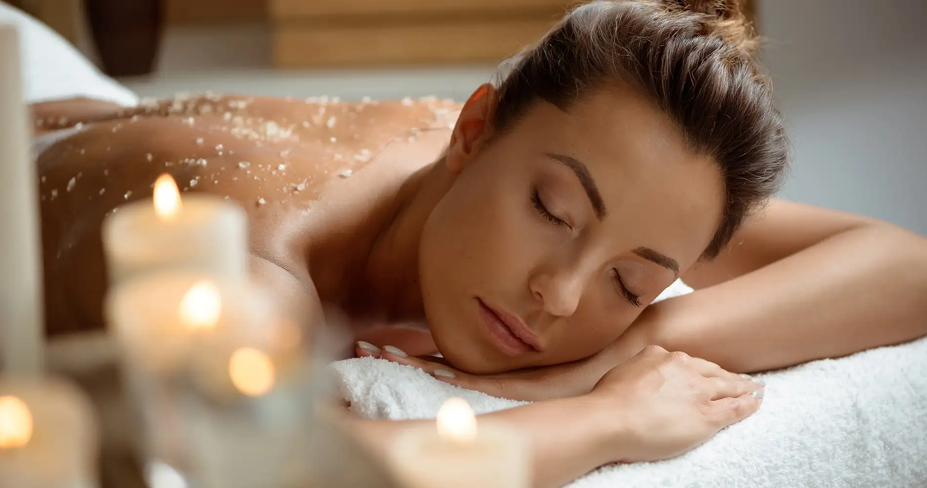 Mujer relaj&aacute;ndose en spa, con velas encendidas y toalla en el rostro