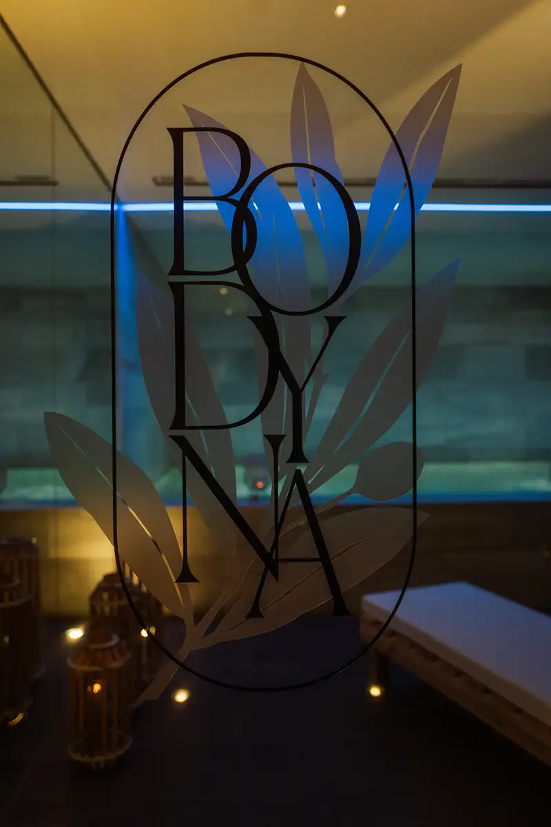 Logo &ldquo;B&Oslash;NY&rdquo; con elementos abstractos azules y fondo de piscina interior
