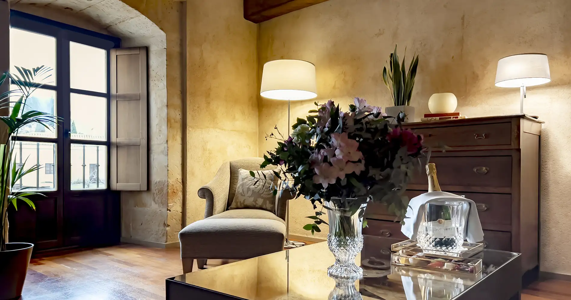 Sala de estar luminosa con sof&aacute;, l&aacute;mparas y flores en jarr&oacute;n cerca de ventana.