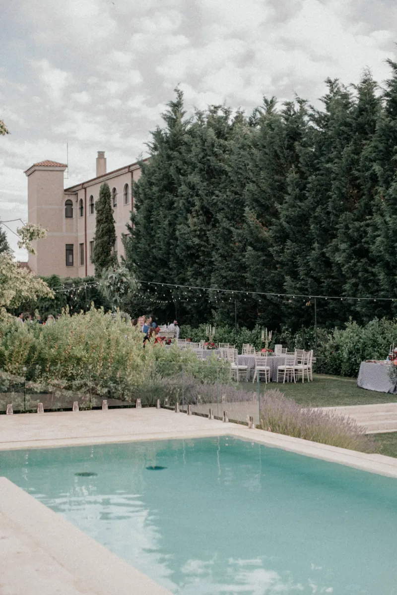Piscina en jard&iacute;n con sillas y un edificio de fondo bajo cielo nublado