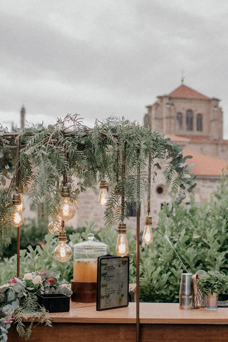 Mesa con luces colgantes y plantas, iglesia de fondo al atardecer