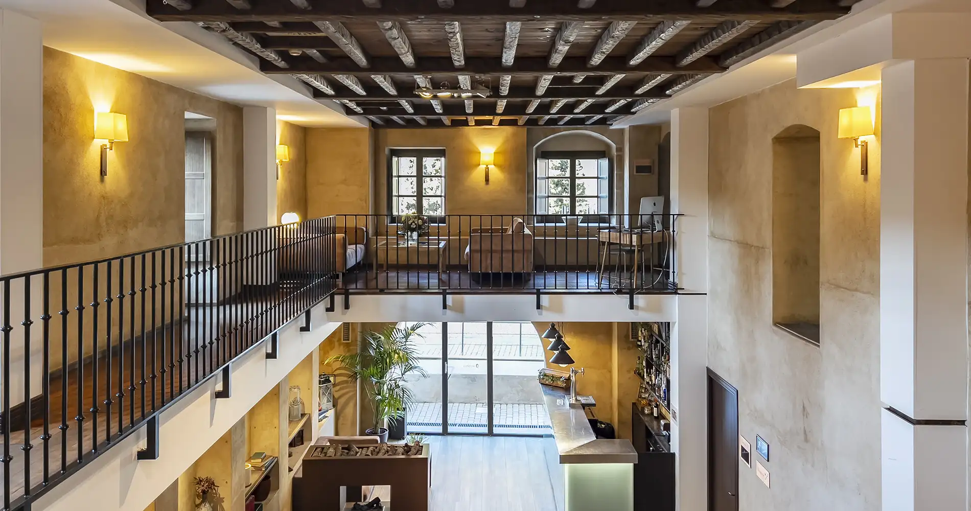 Pasillo interior con doble altura, barandales negros, luces c&aacute;lidas y ventanas