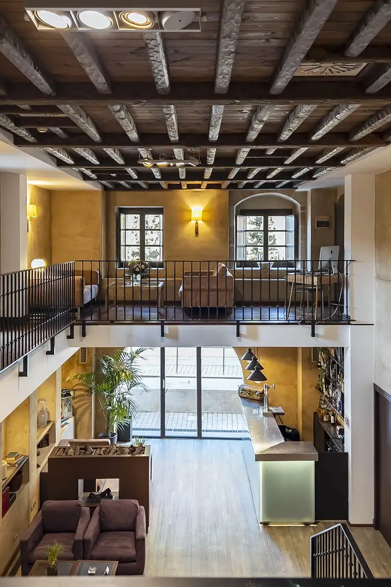 Pasillo interior de estilo r&uacute;stico con techo de vigas, balc&oacute;n y iluminaci&oacute;n c&aacute;lida