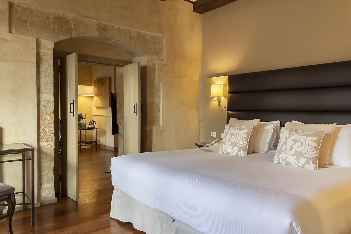 Dormitorio elegante con cama blanca, cojines y l&aacute;mparas, estilo r&uacute;stico.