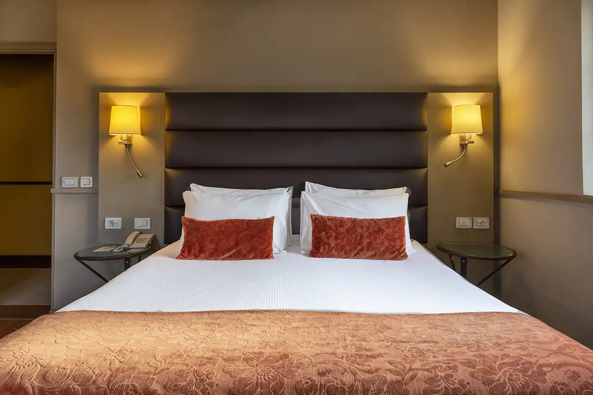 Habitaci&oacute;n de hotel con cama, almohadas rojas y luces de pared c&aacute;lidas