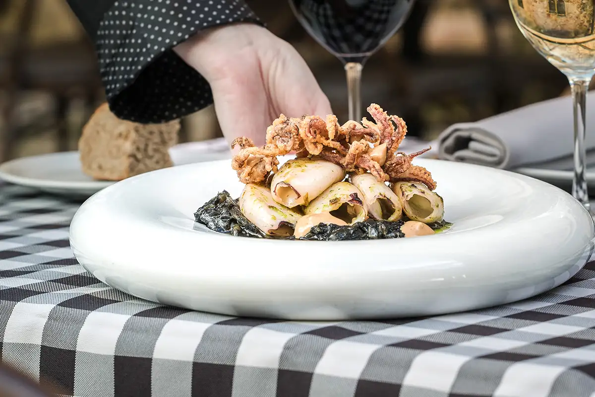 Plato de aperitivo con rollitos de calamar y crumble de carne, vino al lado