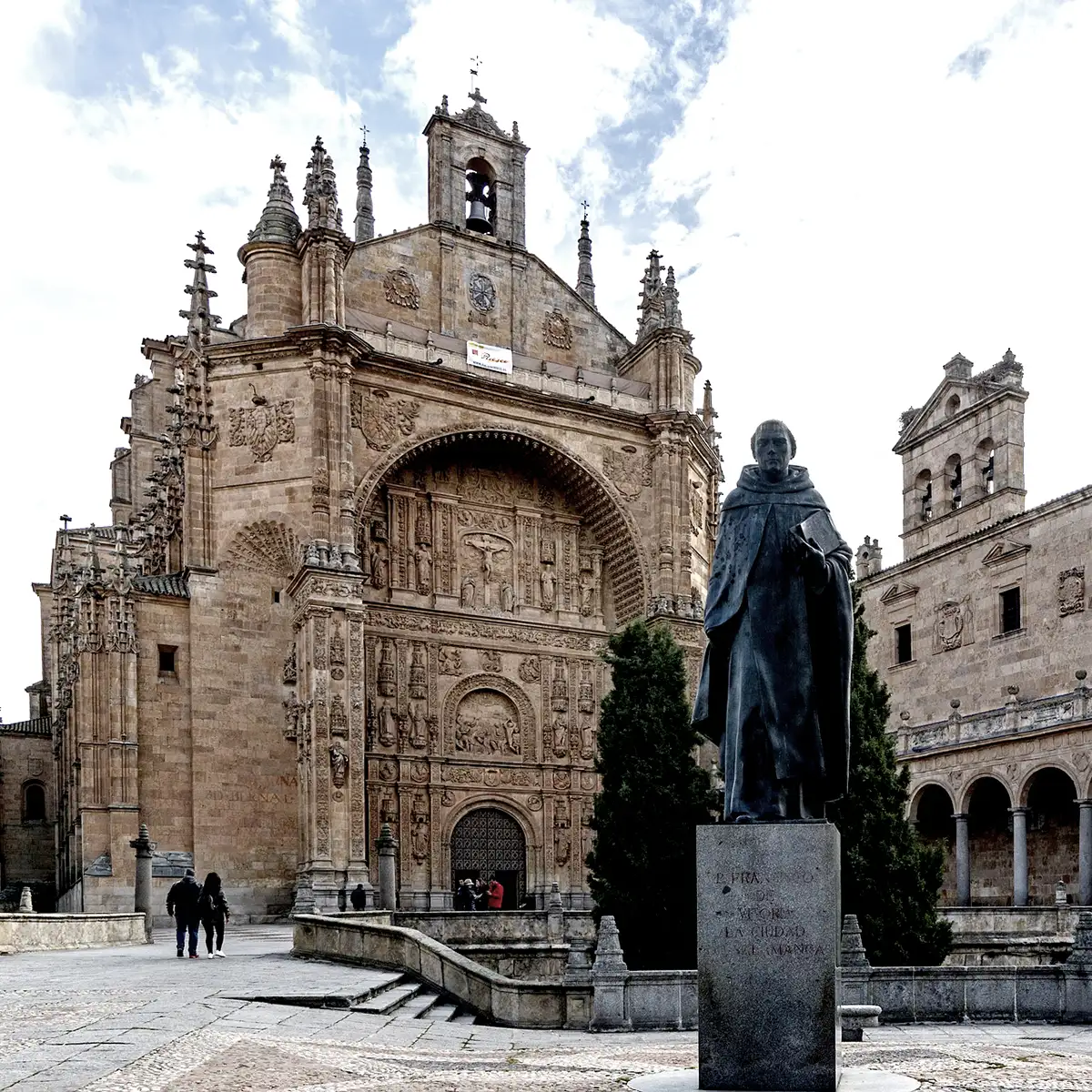 Estatua de bronce frente a una gran iglesia de piedra con campanario y campana