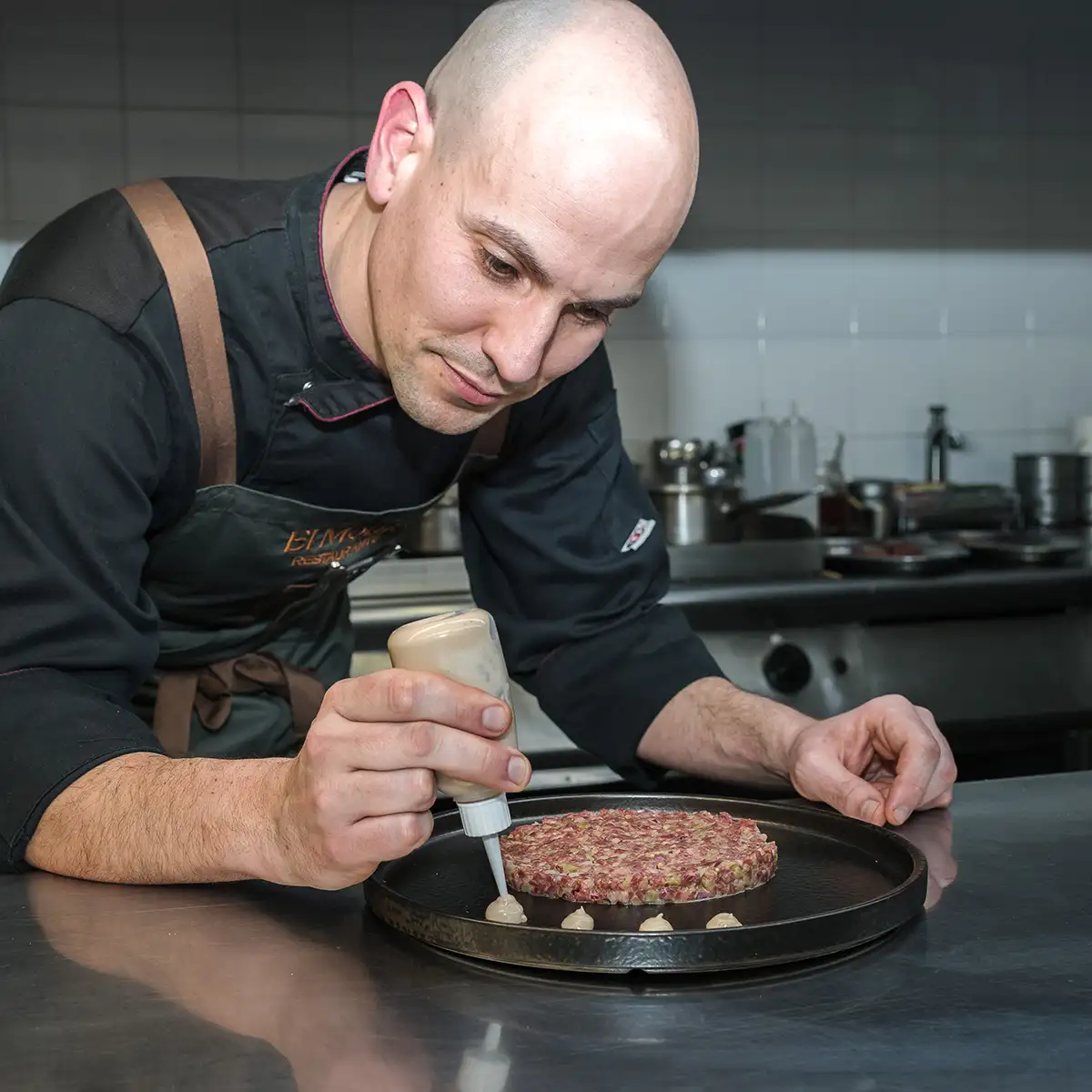 Cocinero prepara hamburguesa con salsa sobre una plancha caliente