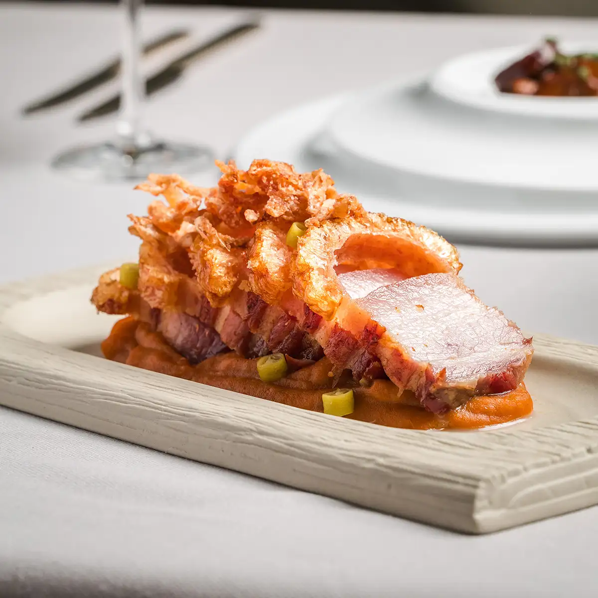 Taz&oacute;n de carne crujiente y salsa con verduras verdes sobre plato blanco