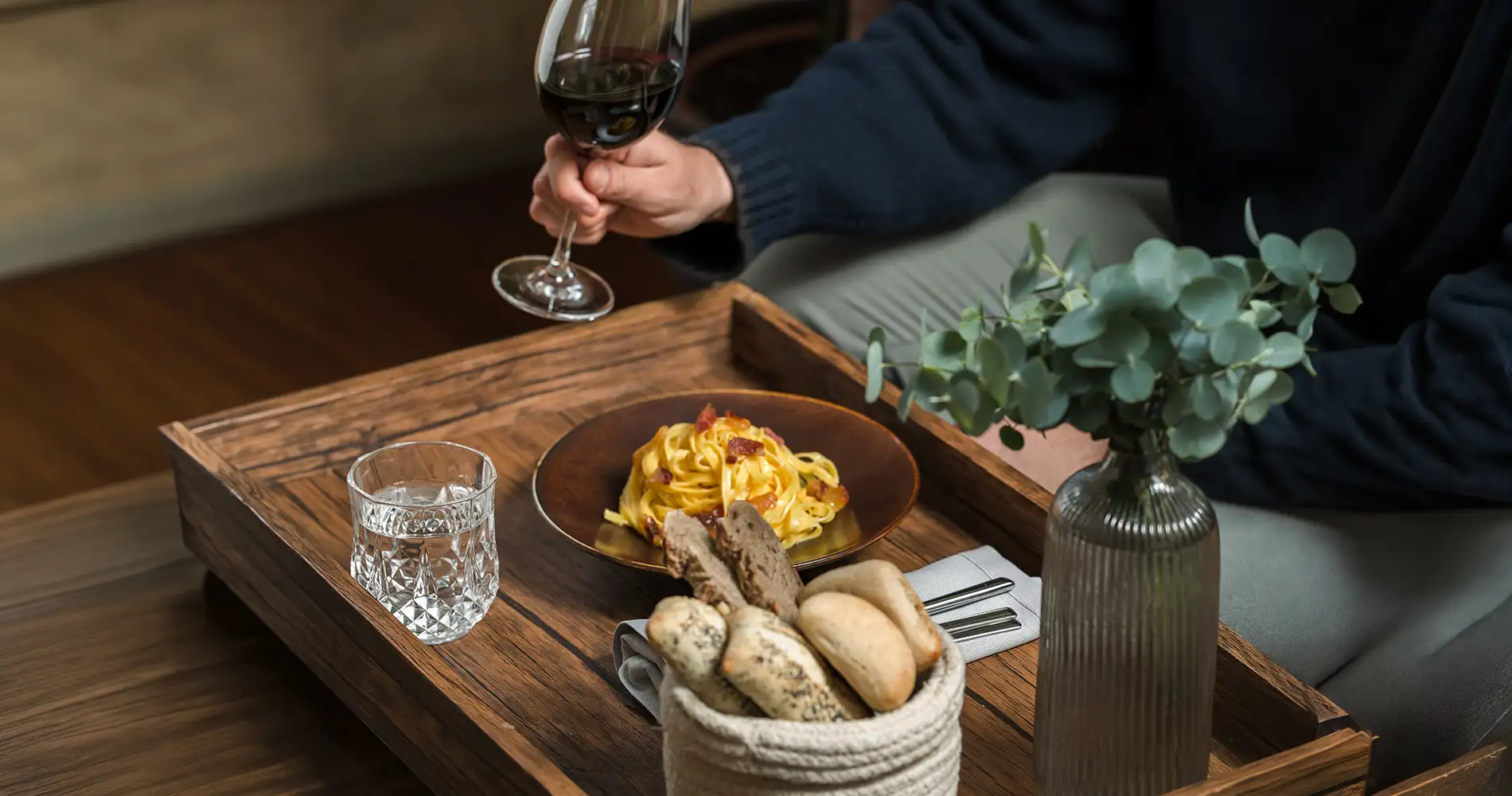 Mano sirviendo vino en mesa con platos de pasta y pan, ambiente elegante